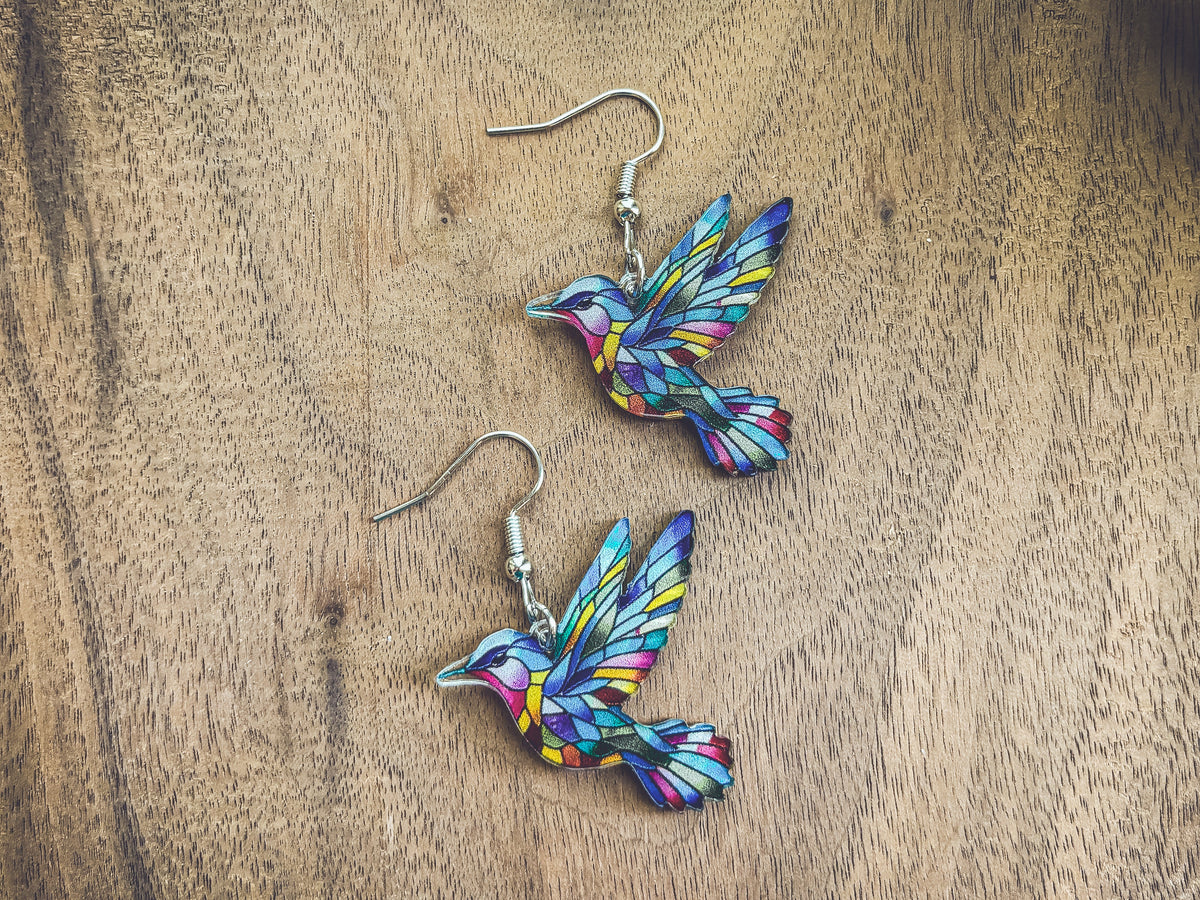 Two colorful hummingbird earrings with silver fishhook and dangle design on wood.