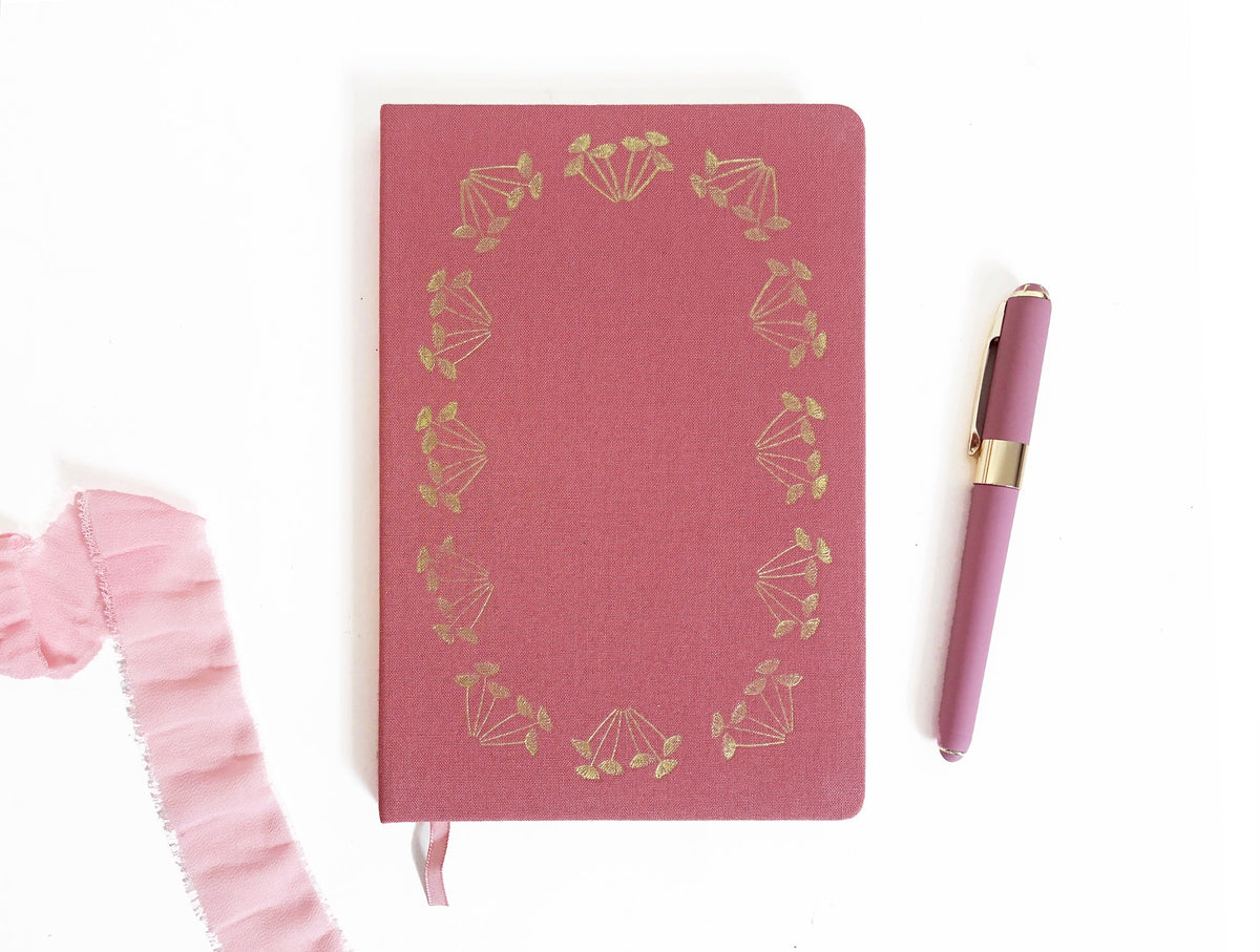 Pink linen-look notebook with gold foil botanical wreath design and ribbon tie
