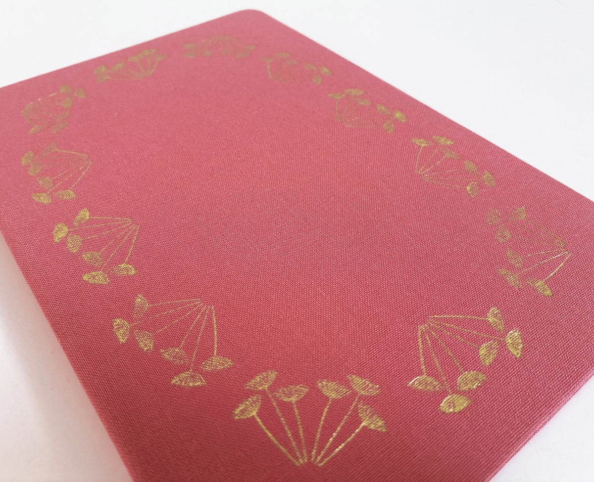 Close-up of pink linen-look notebook cover with gold foil floral wreath