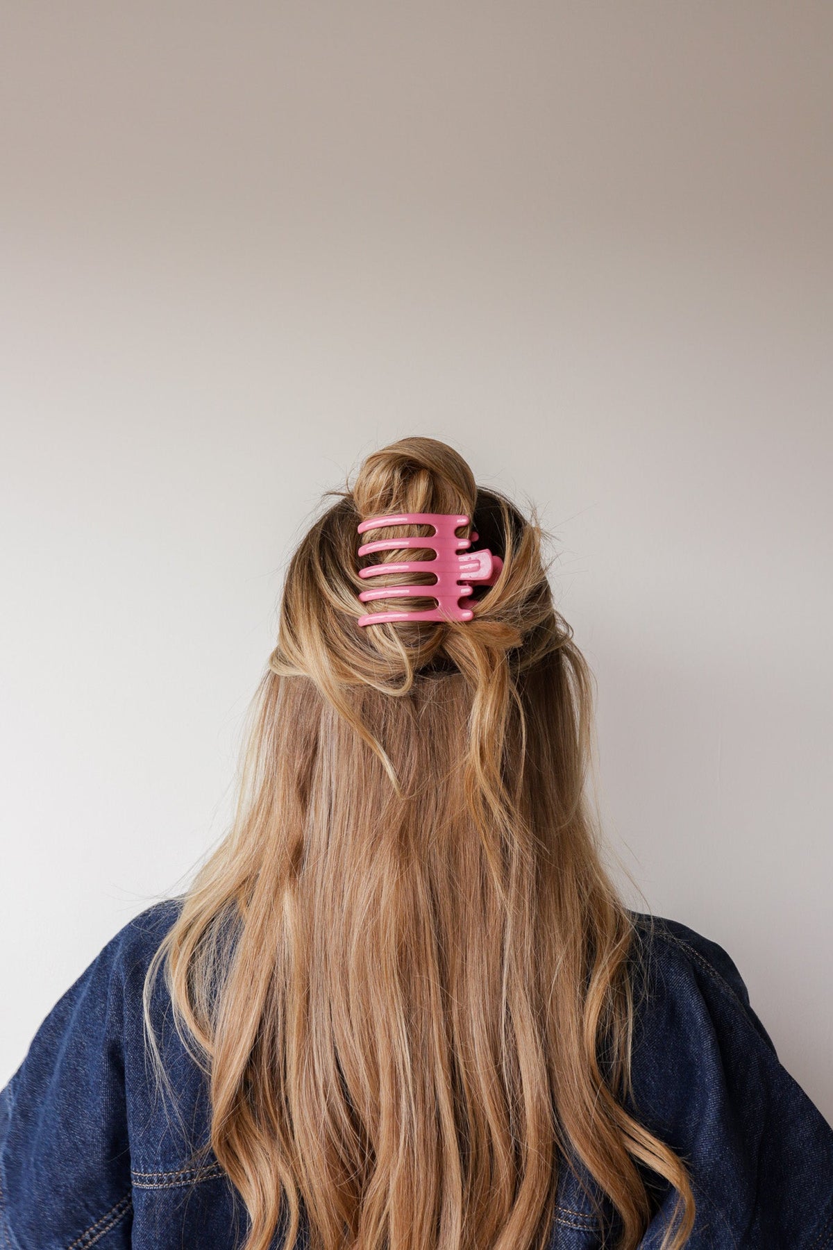 Wide lay-down hair claw, shiny pink; holds long blonde hair in a low bun