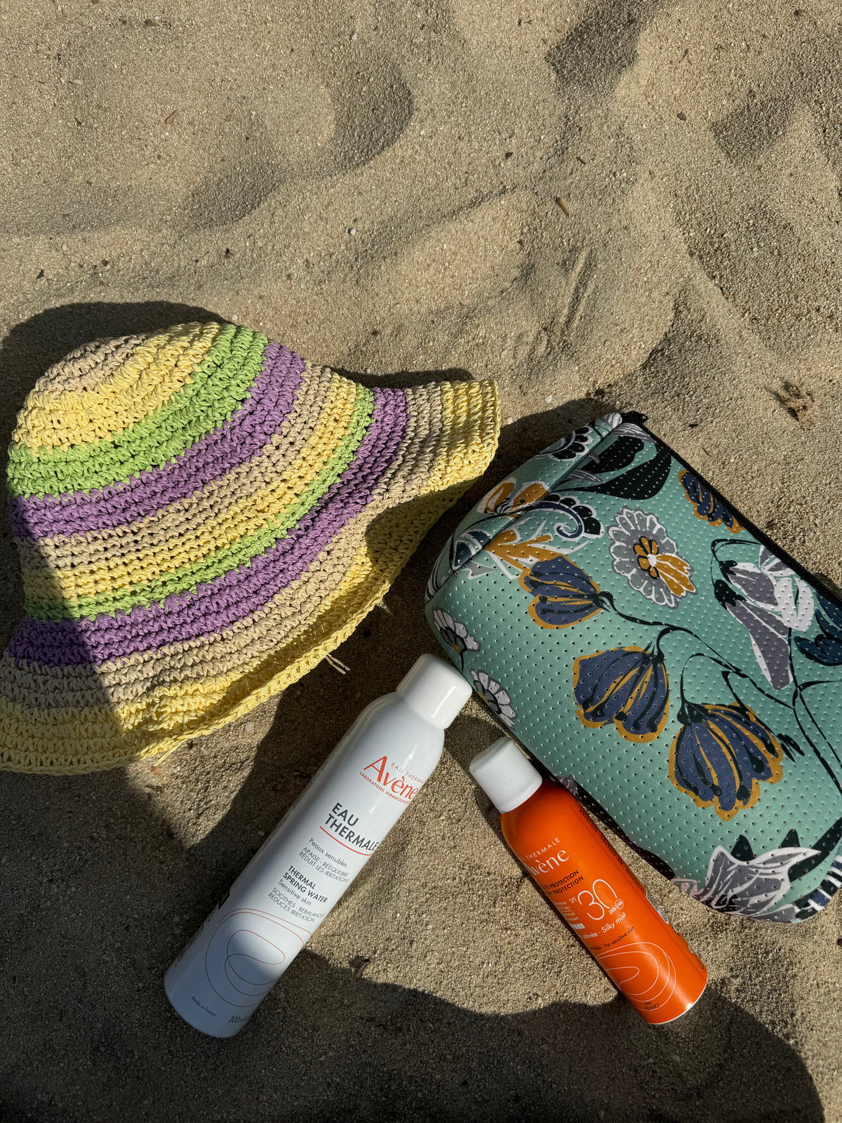 Mint patterned pouch lying on sand with black zipper edge and metal loop