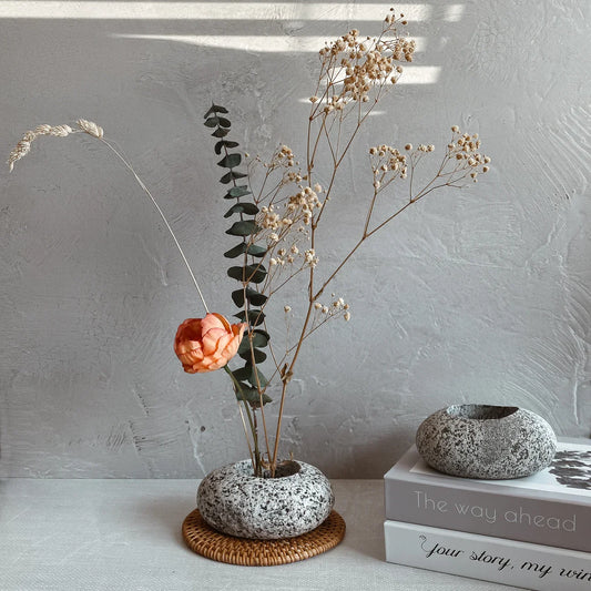 Speckled stone ikebana vase with rounded bowl opening on wicker base ring