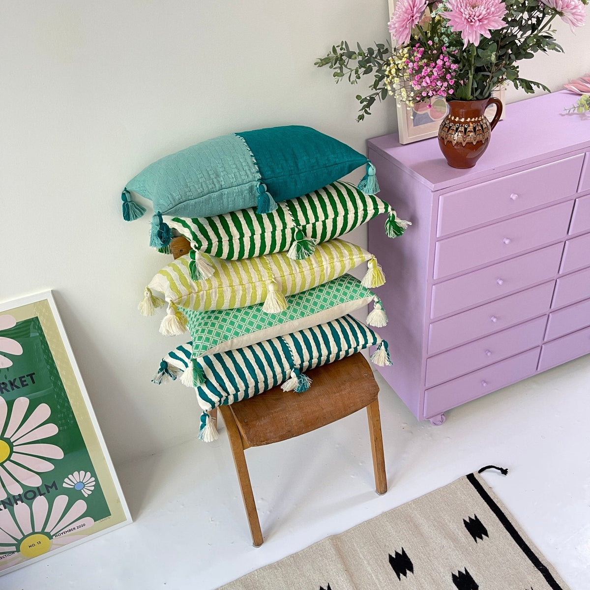 Stacked throw pillows in teal, green-striped, and yellow with tassel trim