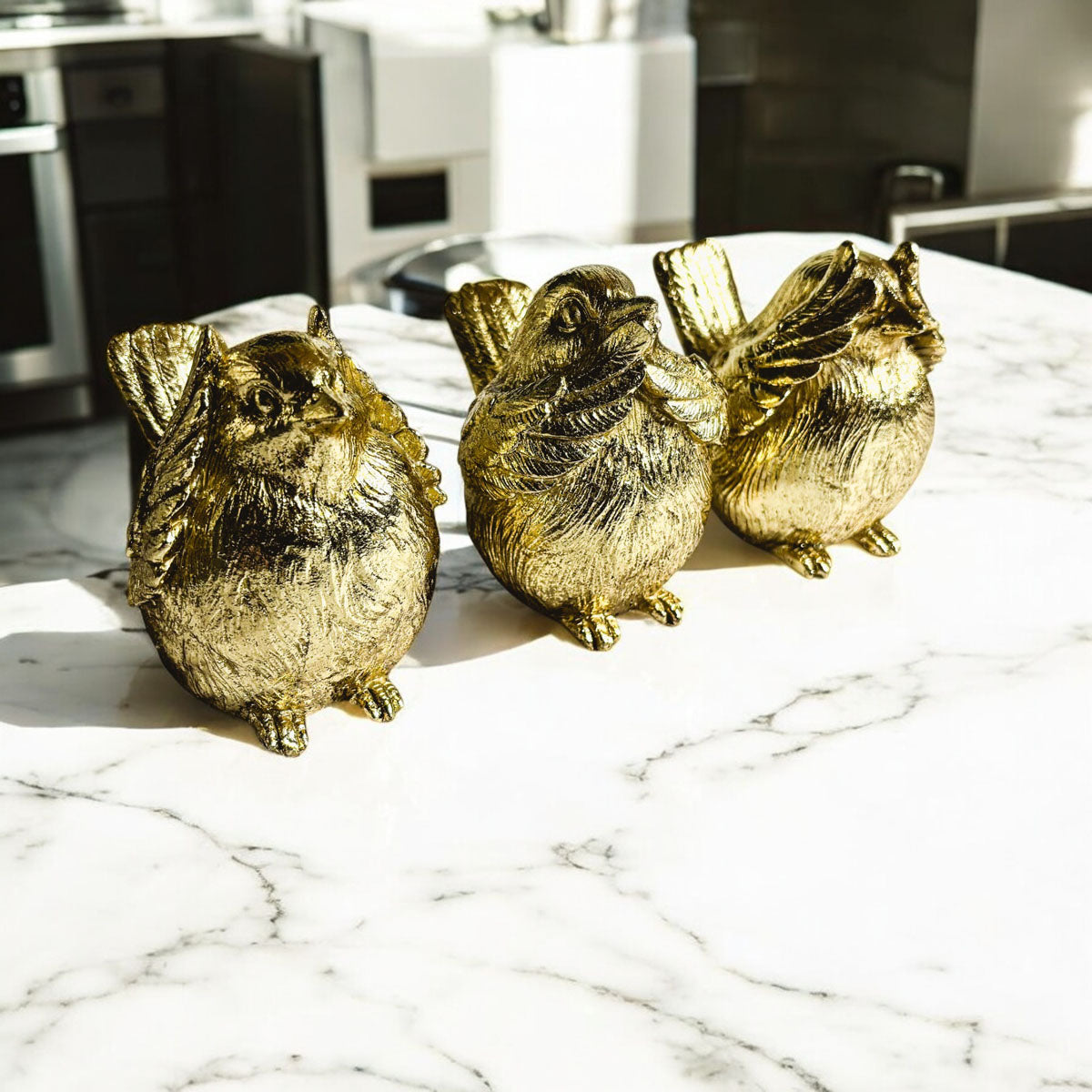 Golden three wise birds figurines, standing on a marble surface.