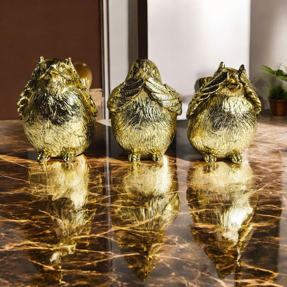 Three golden wise bird figurines standing on a reflective table.