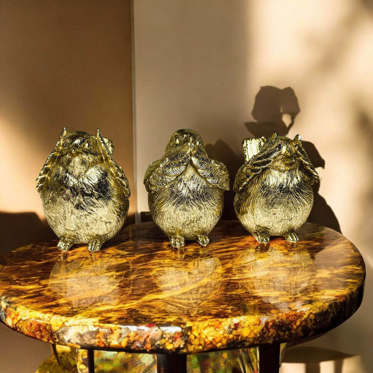 Three gold-tone bird figurines standing on a round wooden table