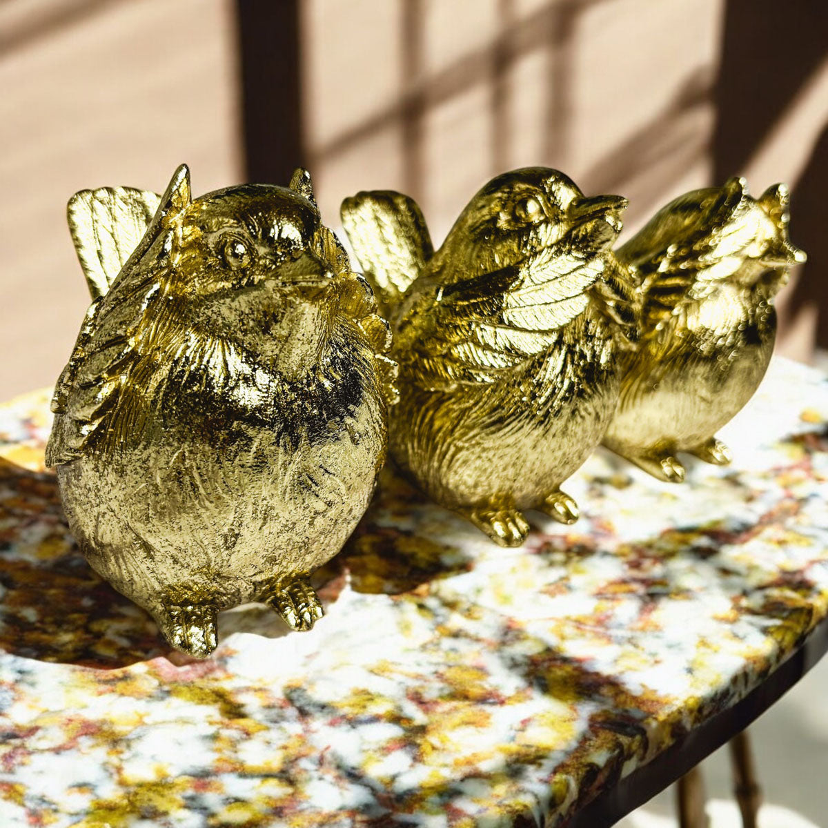 Three gold-tone bird figurines with wings raised on a patterned tabletop