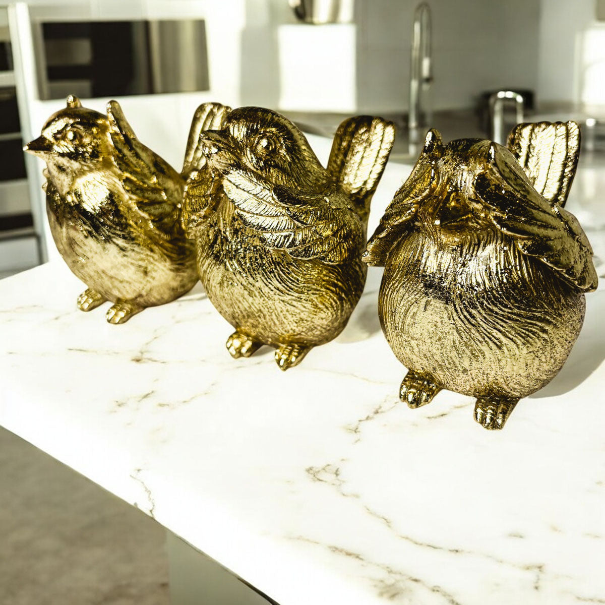 Three gold-tone bird figurines lined up on a white marble counter