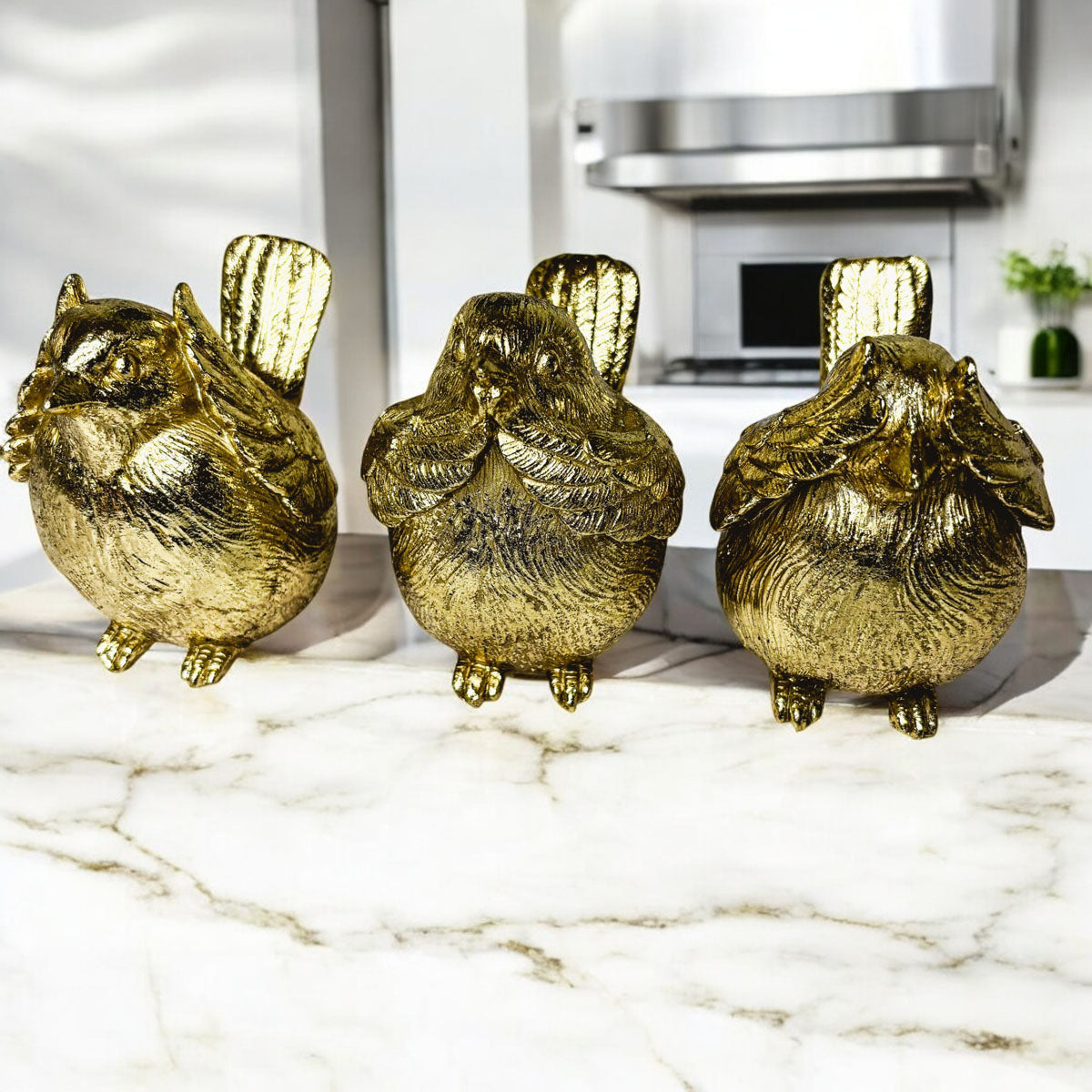 Three gold-tone bird figurines standing together with raised wings and feather texture