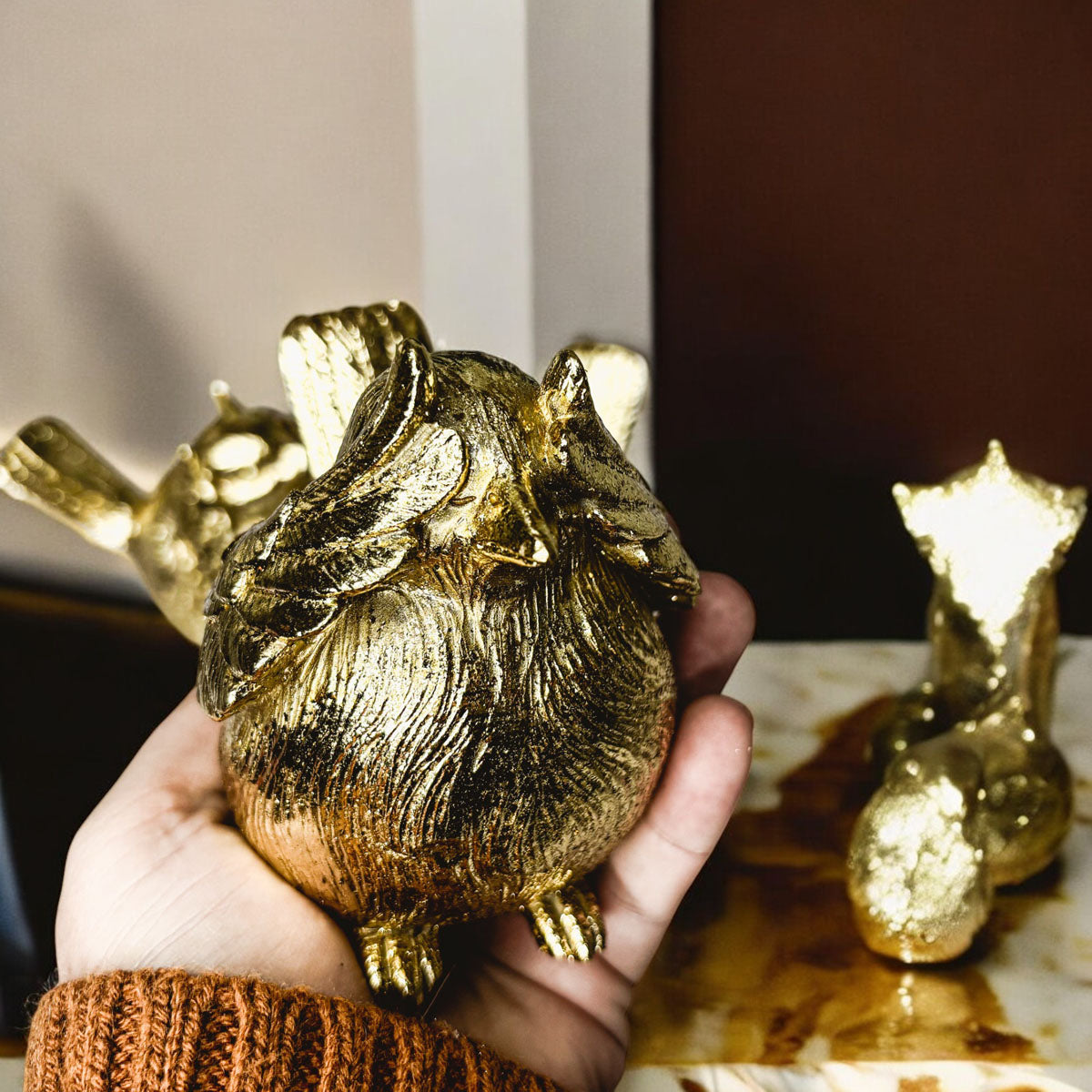 Hand holding a gold-tone bird figurine with textured feathers and wings