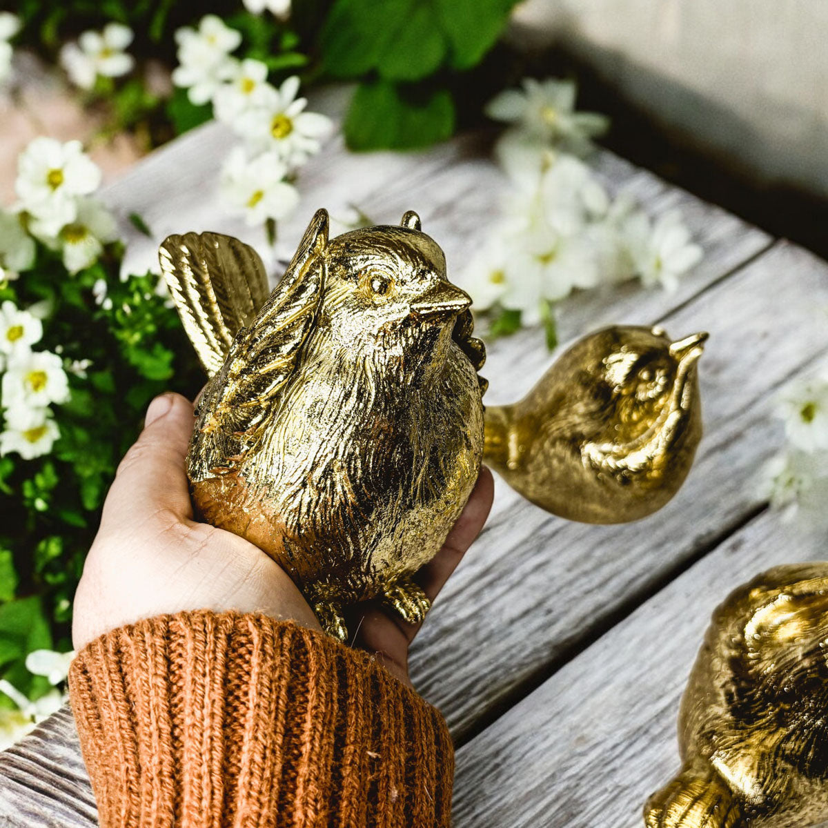 Golden wise bird figurine being held in a hand, with another bird beside it.