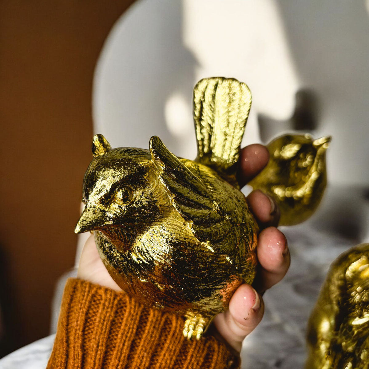 Close-up of a golden wise bird figurine held in a hand.