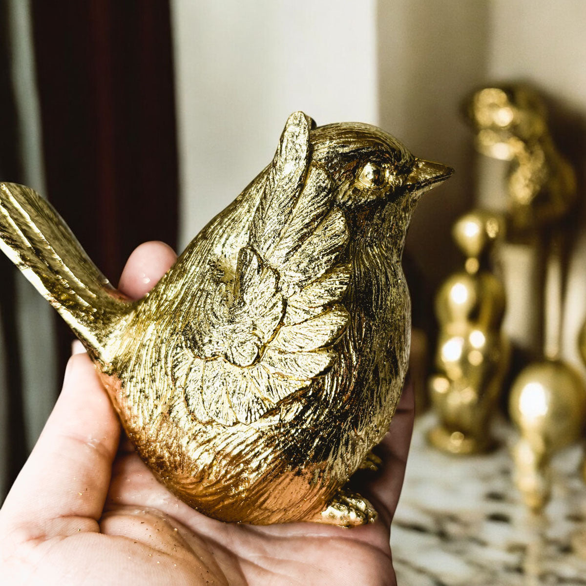 Hand holding a gold-tone bird figurine with detailed feather and wing texture