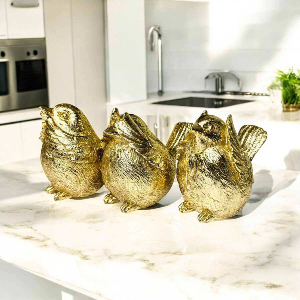 Three gold-tone bird figurines standing side by side on a countertop