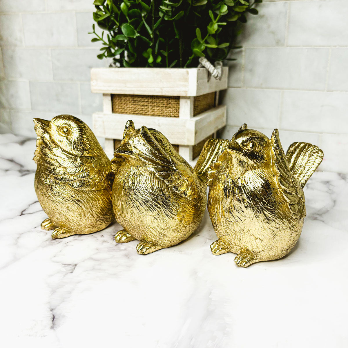 Three gold-tone bird figurines arranged together beside a small plant pot