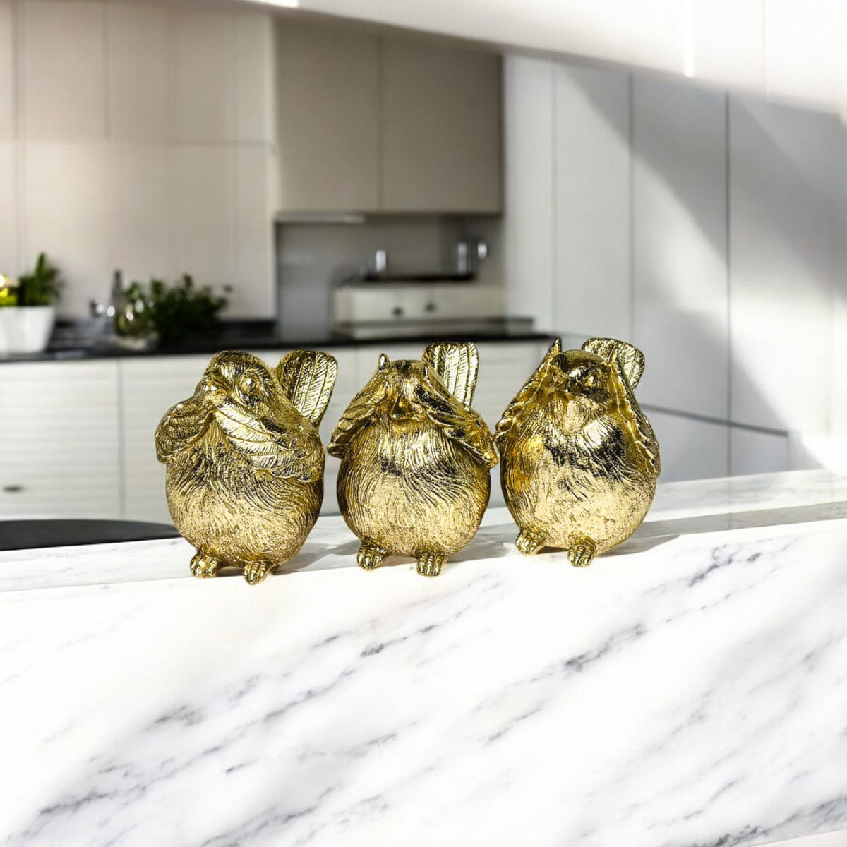 Three golden wise bird figurines standing together on a kitchen countertop.