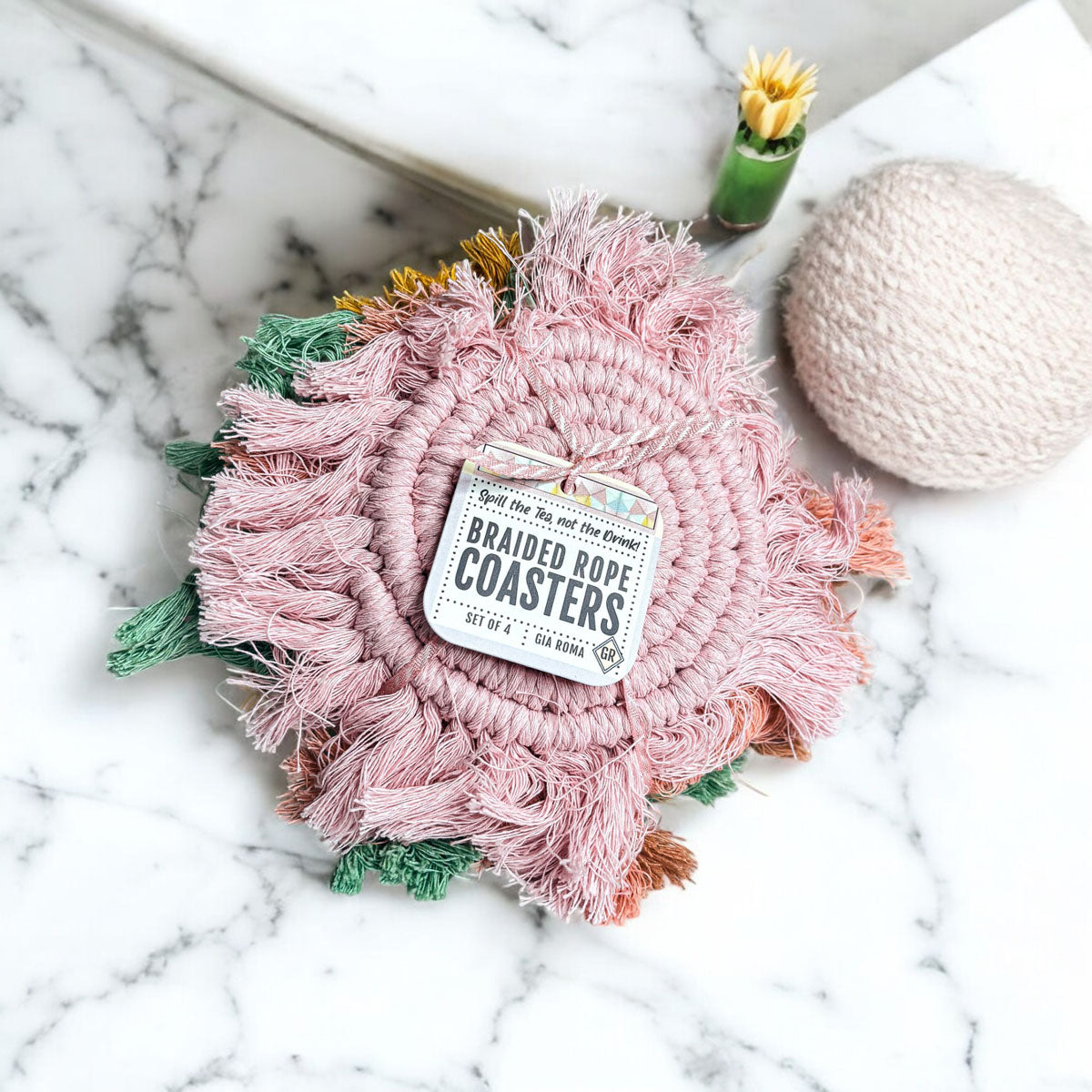 Close-up braided rope tassel coaster in light pink with green and peach tassel accents