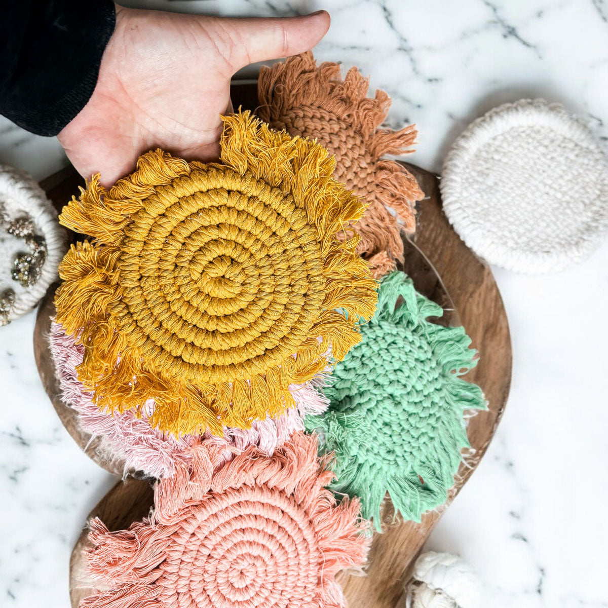 Round braided rope coasters in gold, brown, green, and pale tones with tassels