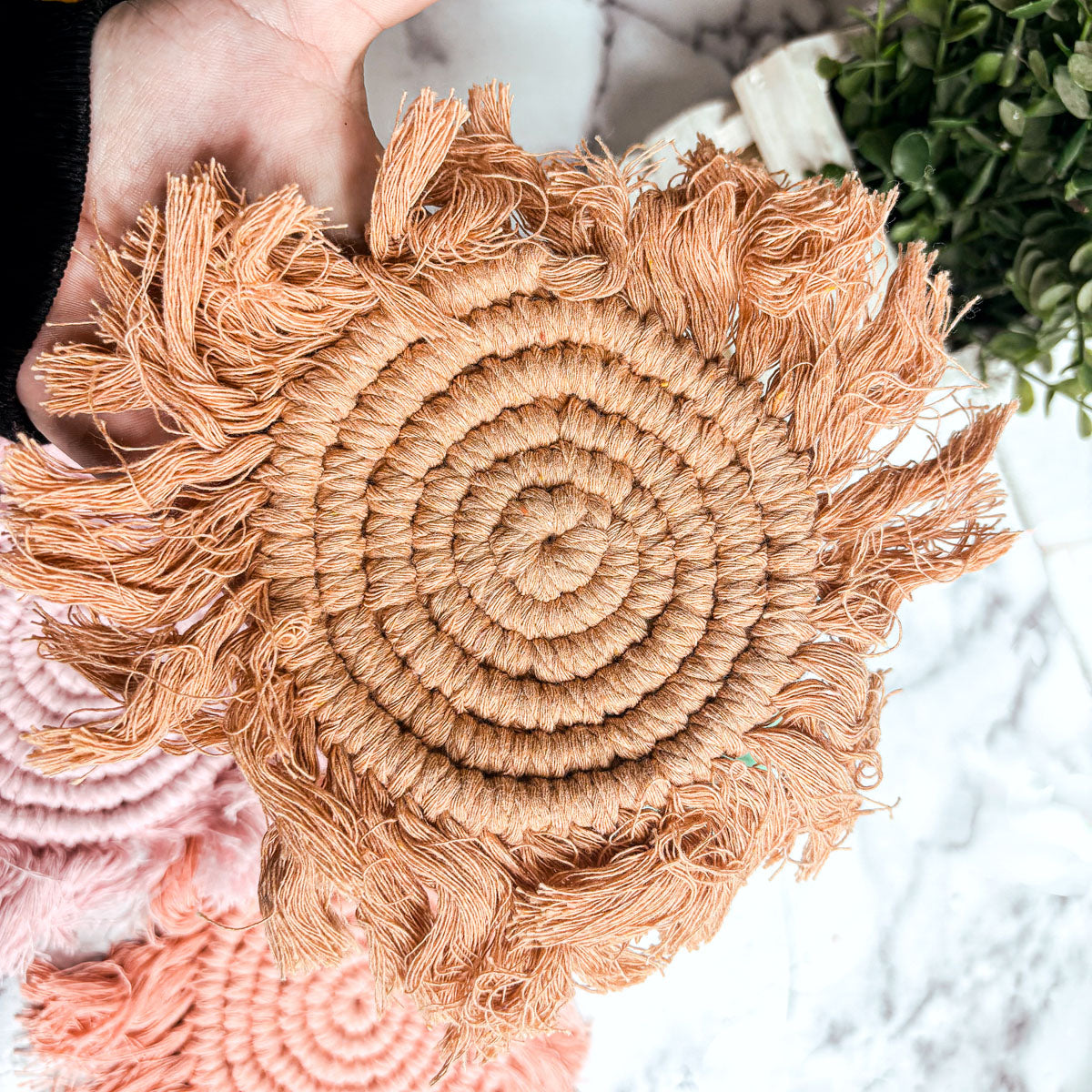 Round braided rope coaster in warm tan with fringed tassels and spiral weave