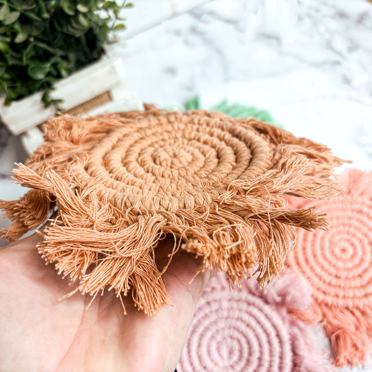 Peach-orange round braided rope coaster with fringed tassels and spiral center