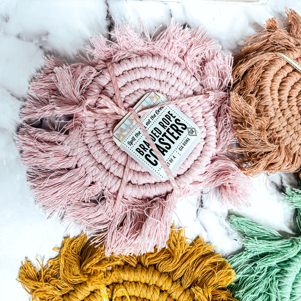 Braided rope tassel coasters set in pink, orange-brown, green, and yellow with round labels