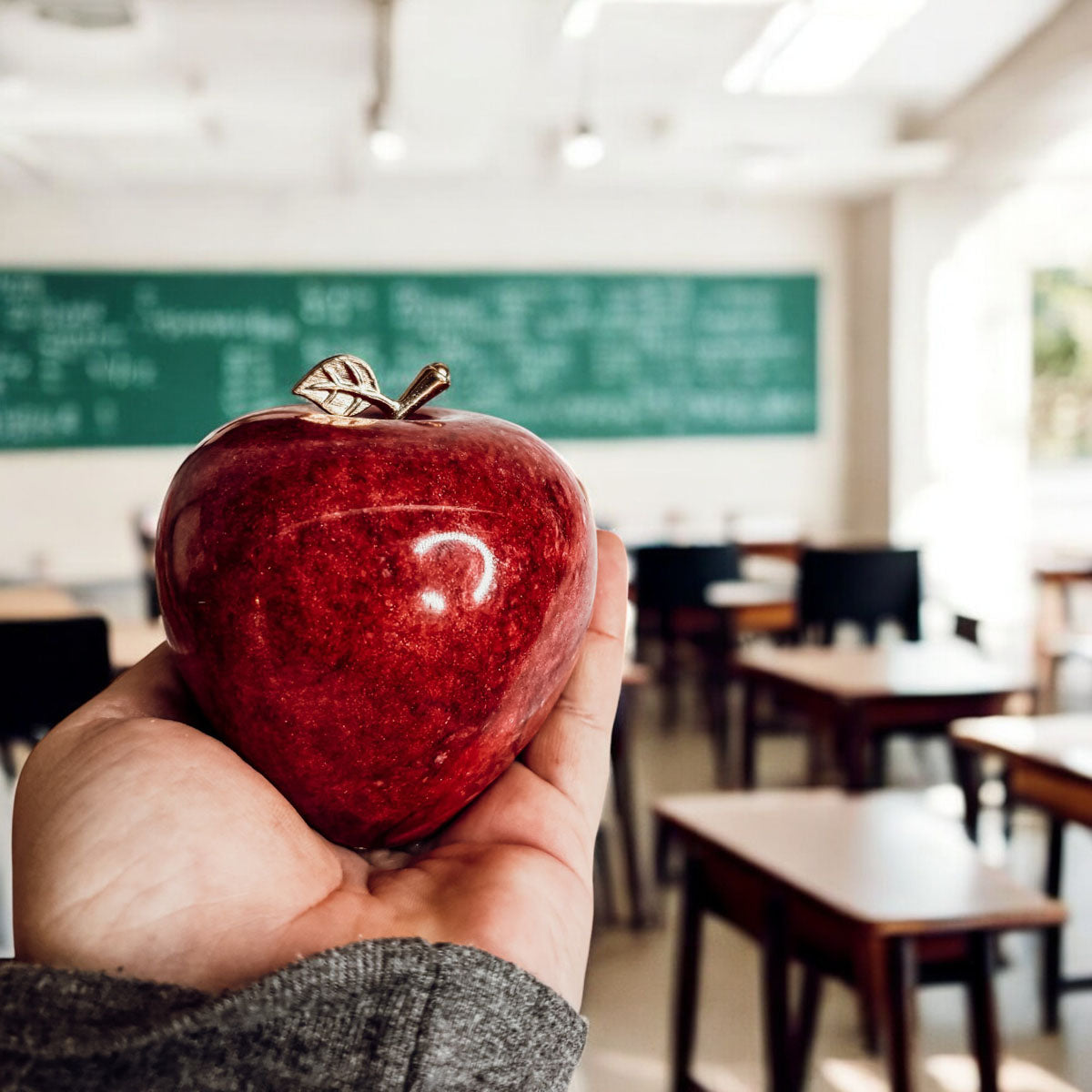 Hand holding a red stone apple paperweight with gold-tone crown top