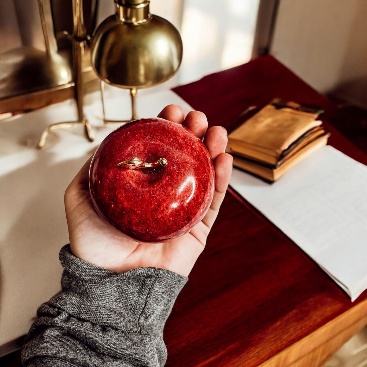 Hand holding a red stone apple paperweight with gold-tone top detail