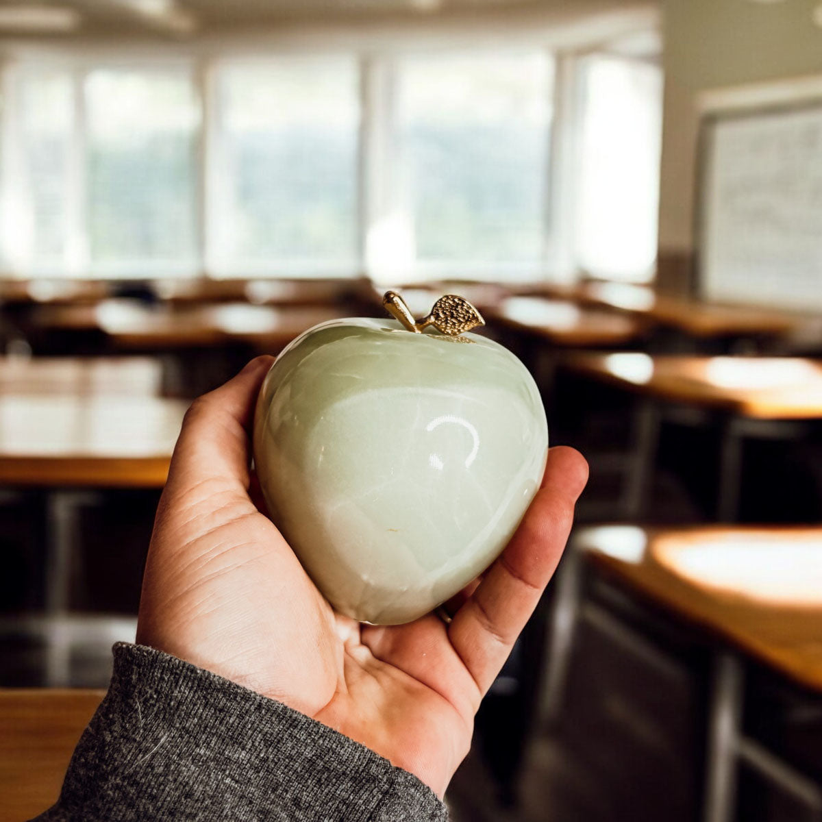 Light green heart-shaped paperweight with gold top clasp, held in a hand.