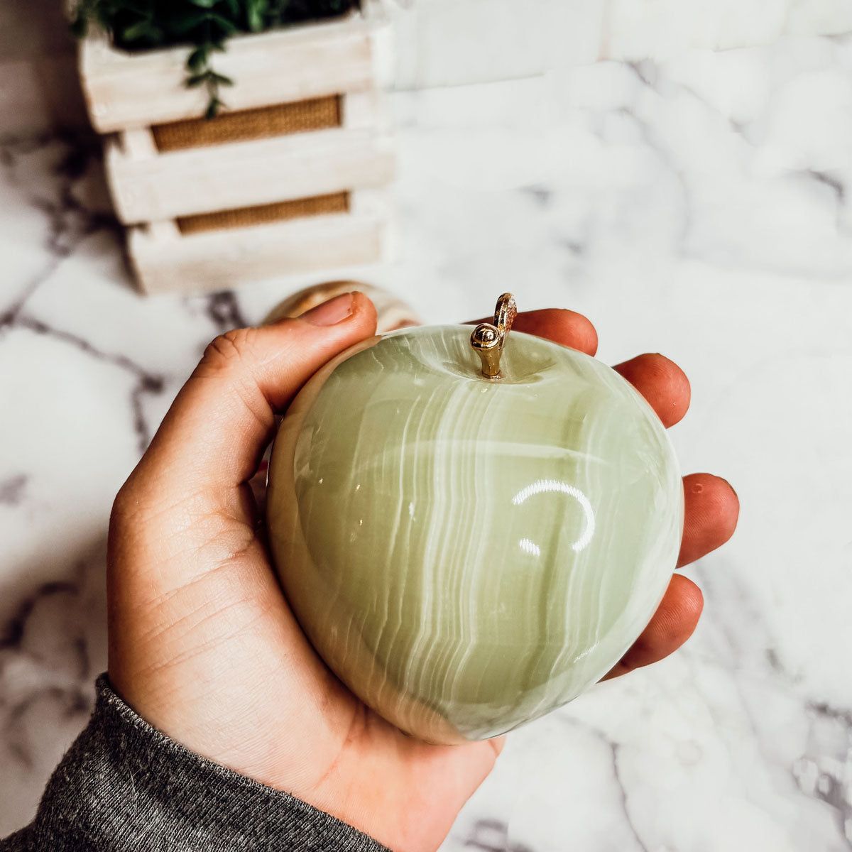 Olive green heart-shaped paperweight held in hand with gold top clasp.