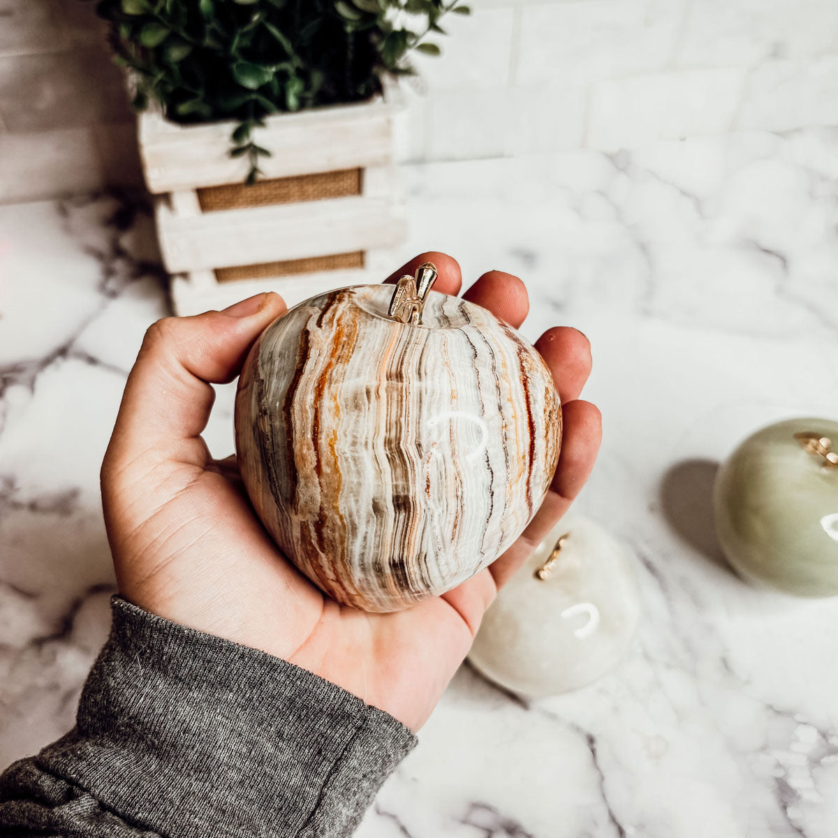 Agate stone apple paperweight held in hands with gold-tone crown top