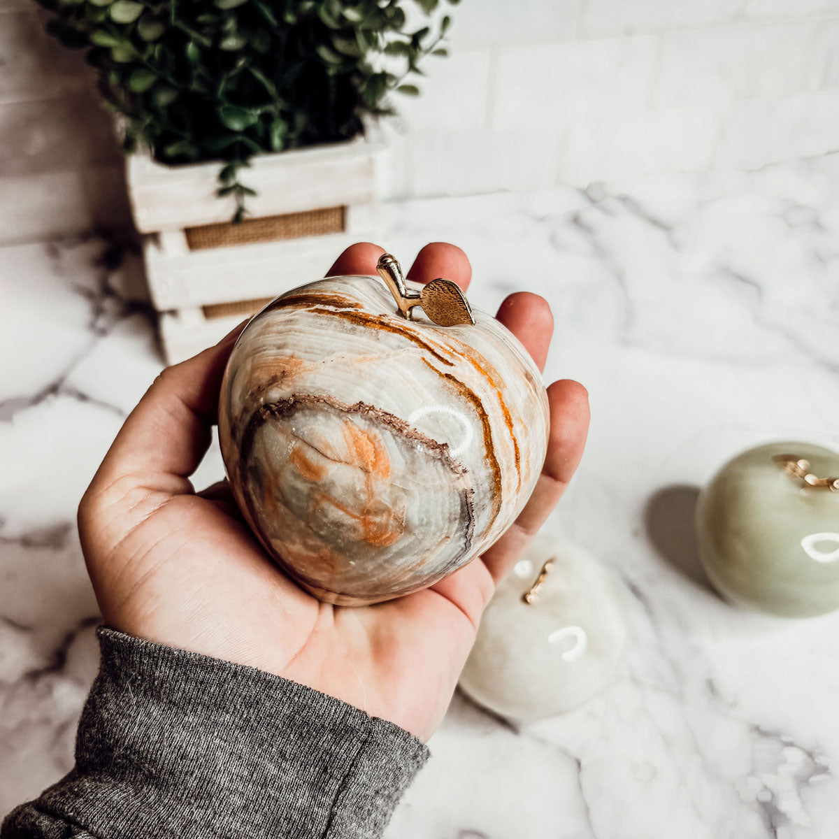 Hand holding an agate stone apple paperweight with gold-tone crown top