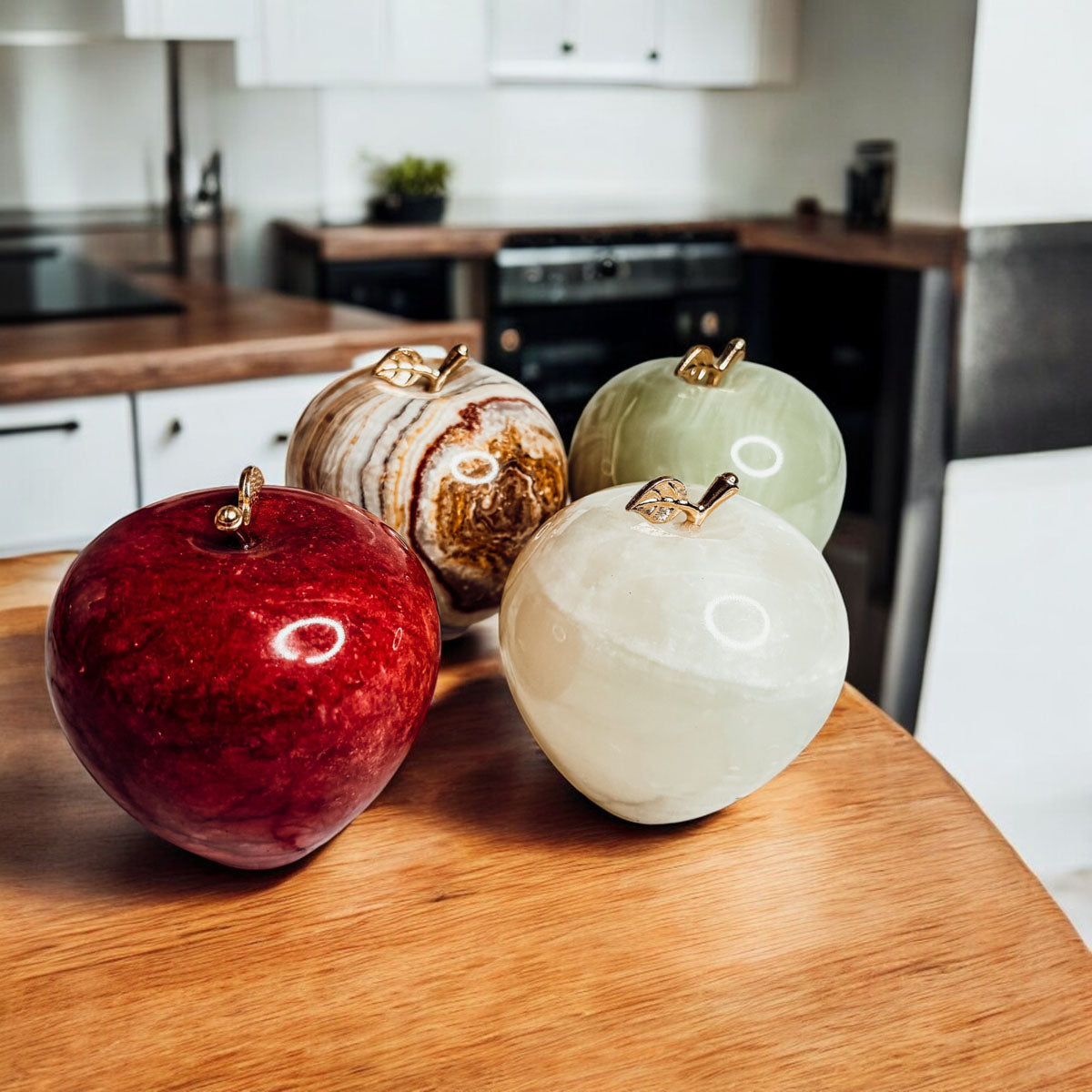 Apple-shaped stone paperweights on a wooden surface in red, agate, white, and green onyx