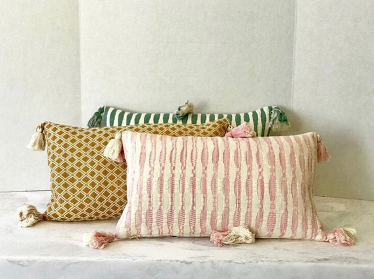 Faded pink striped pillow with corner tassel pom-poms on a bench