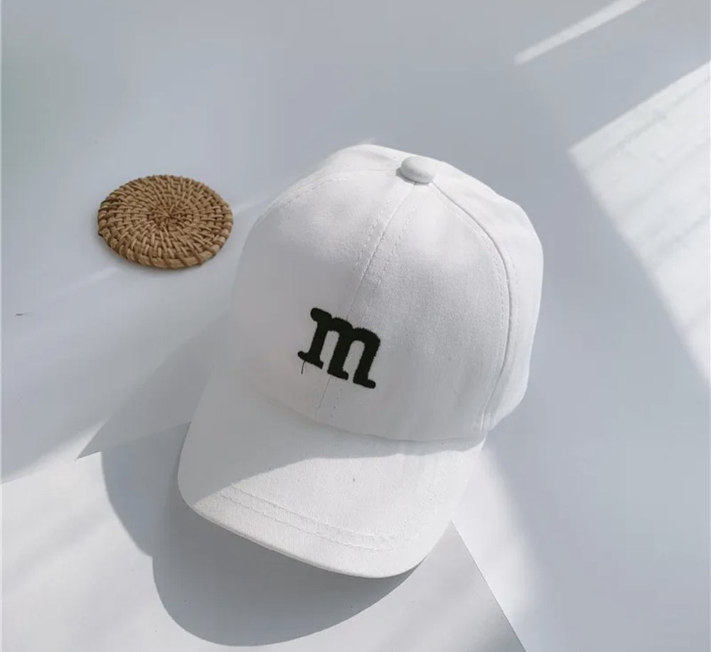 Kids baseball cap in white with a black “m” logo on the front