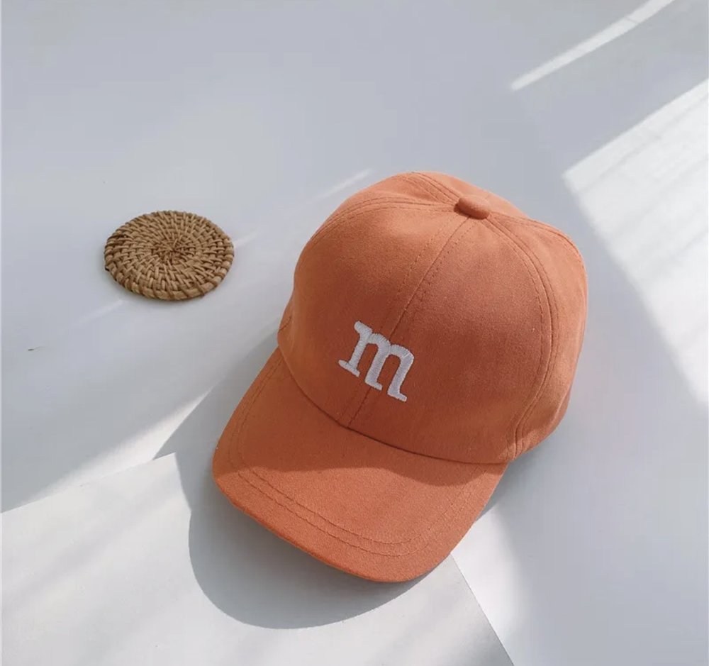 Kids baseball cap in orange with an “m” logo embroidered on the front