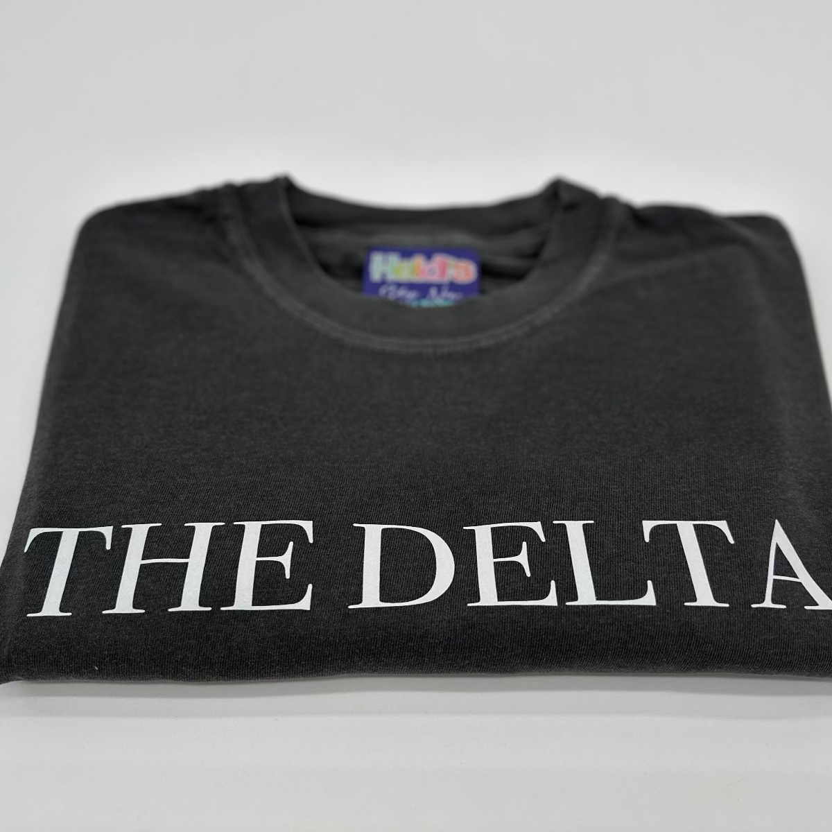 Dark charcoal crew-neck graphic T-shirt with large white “THE DELTA” lettering across chest.