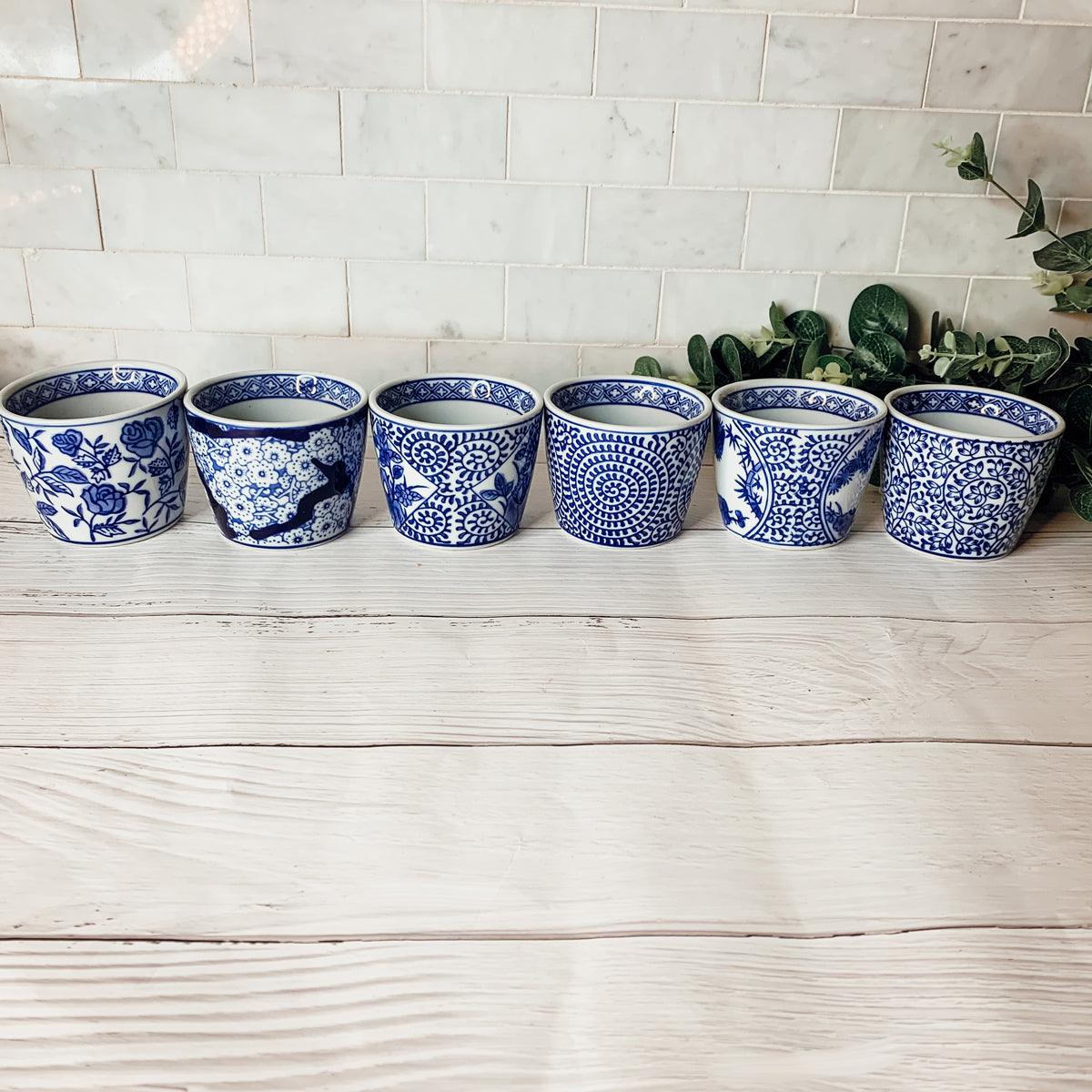 Row of small blue-and-white ceramic cachepots with greenery cuttings