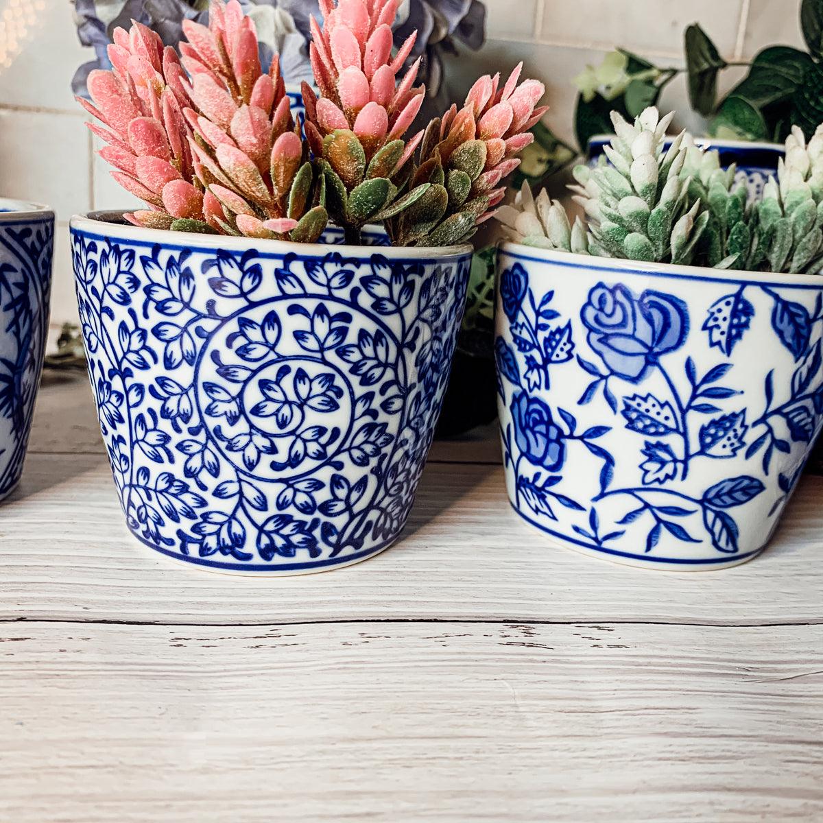 Two blue-and-white ceramic cachepots holding pink and green faux succulents
