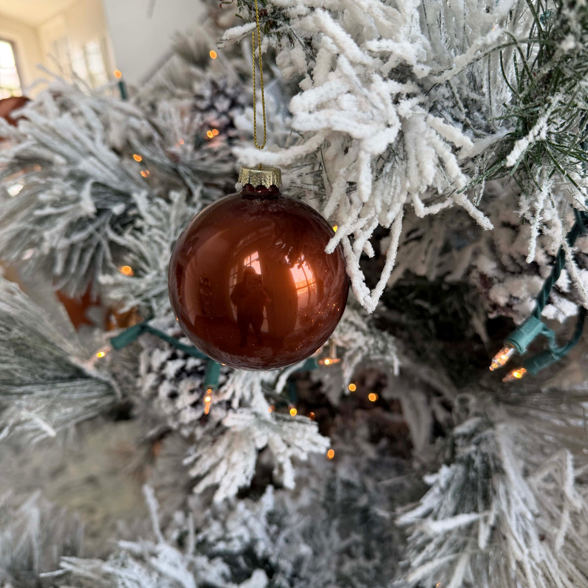 Deep brown glass ornament ball with gold cap hanging on a snowy Christmas tree