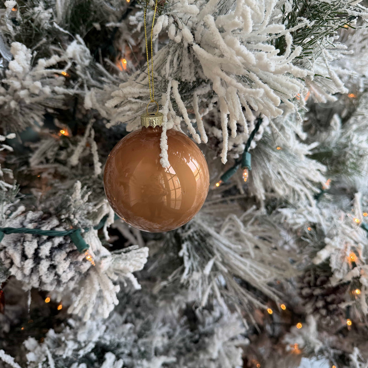 Amber-brown glass ornament ball with gold chain hanging from a snow-covered tree