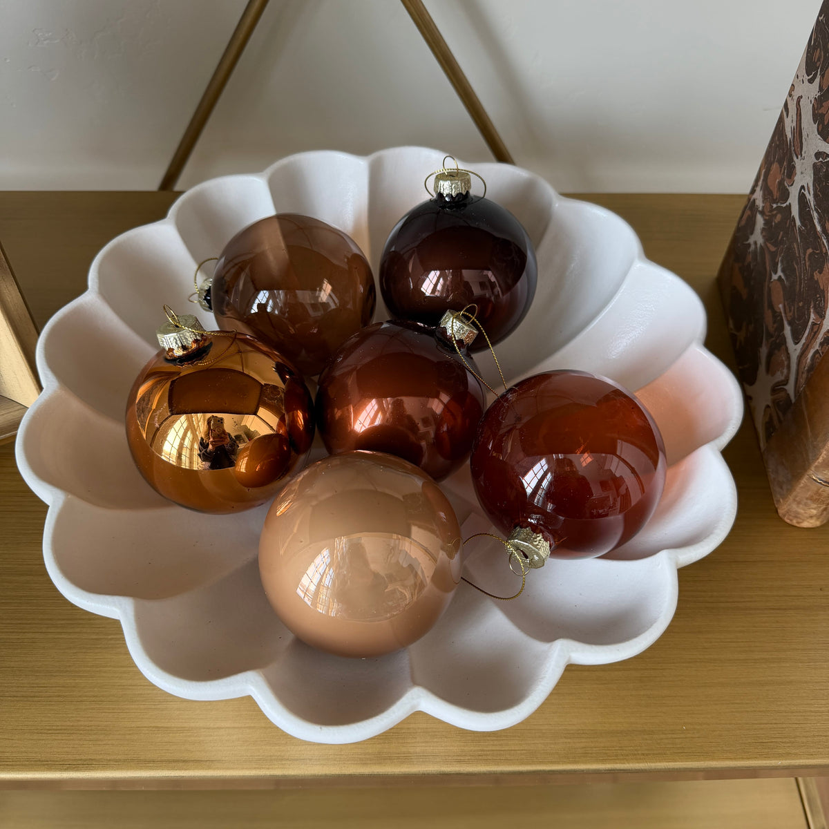 Mixed brown glass ornaments in a white scalloped dish on a wooden shelf