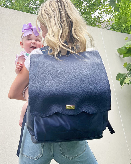 Navy diaper bag backpack worn by a parent, front flap pocket visible