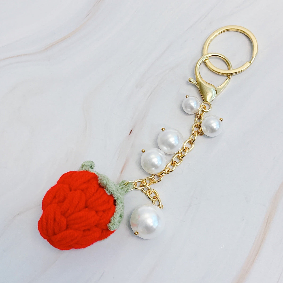 Gold bag charm with red pom-pom strawberry, green leaf, and white pearl beads on chain