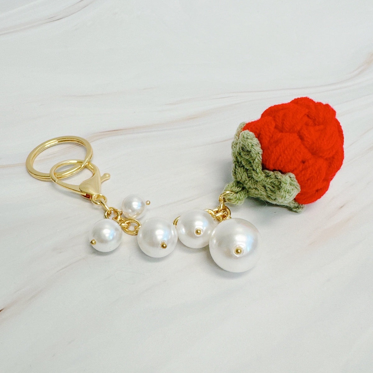 Gold bag charm with red strawberry pom-pom and white pearl drops, green leaf detail