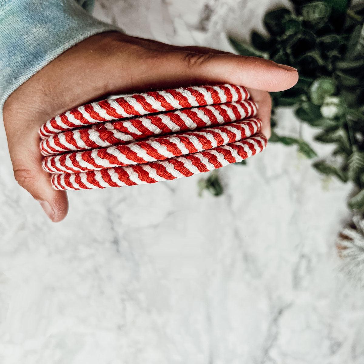 Stack of round woven coasters with red-and-white candy cane stripes, held in hand