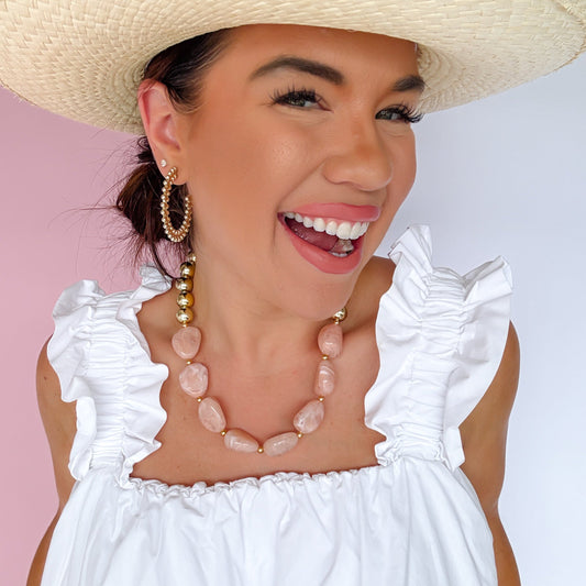 Blush pink bead necklace with gold ball accents, worn with ruffled neckline