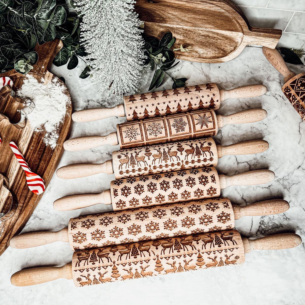 Wood rolling pins stacked on marble with engraved snowflake, reindeer, and holiday motifs