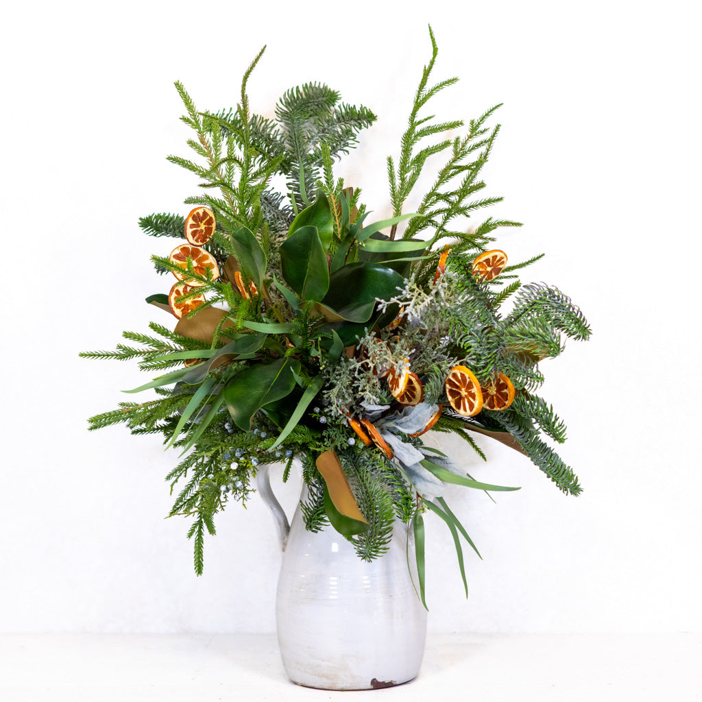 Holiday floral bouquet in a white vase with green foliage and orange slice accents.