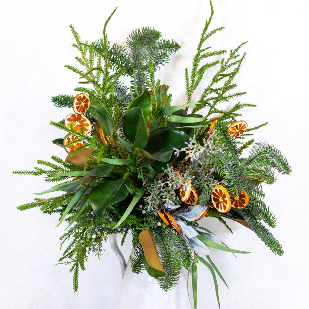 Holiday floral bouquet with green evergreen sprigs, eucalyptus leaves, and orange slice decorations.