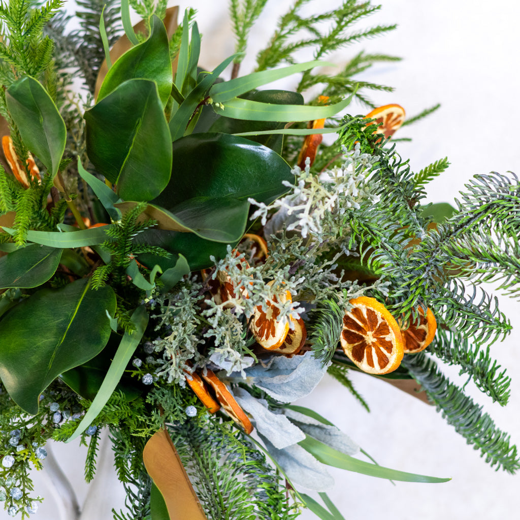 Close-up of holiday bouquet foliage with orange slice charms and light blue ribbon.